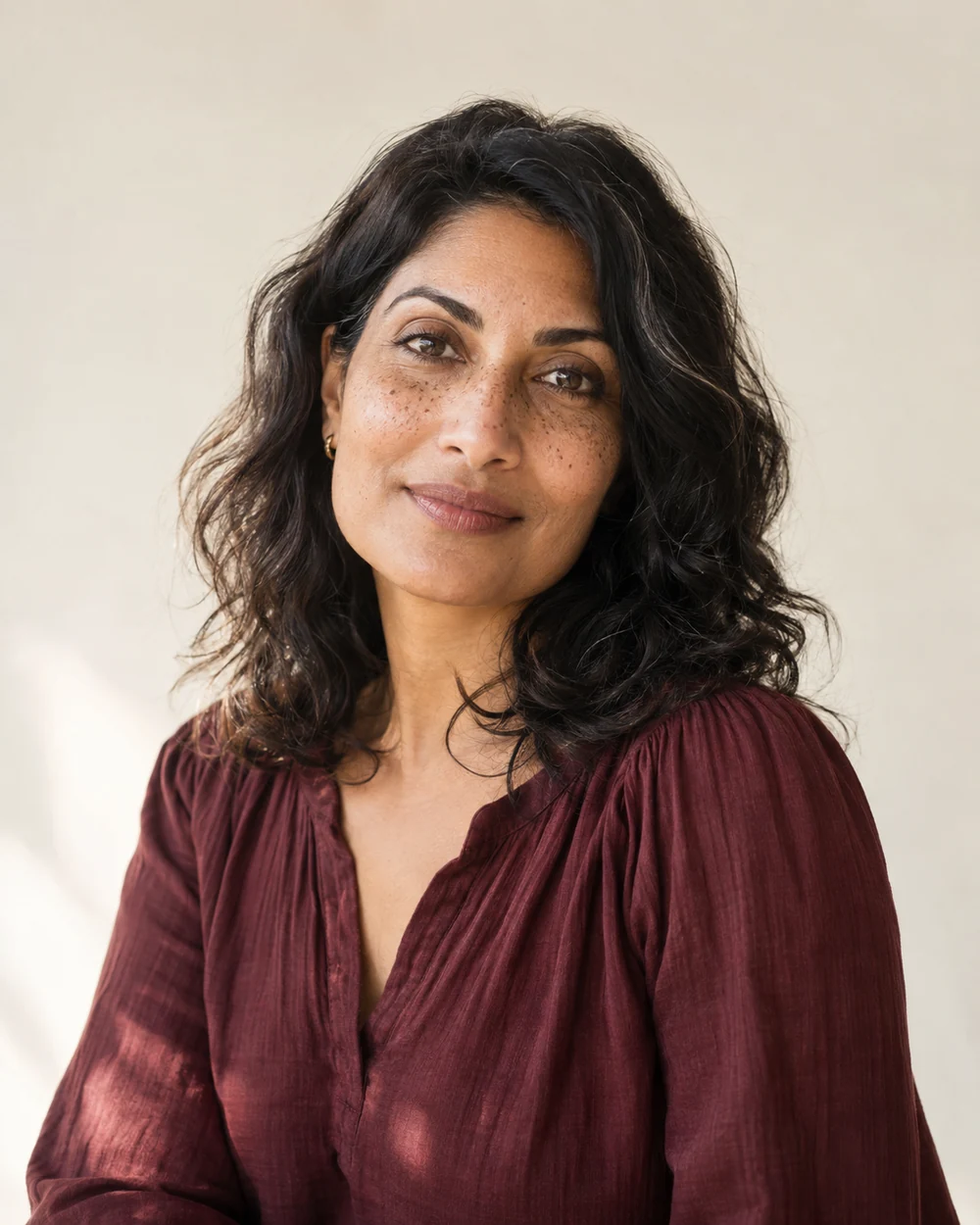 An adult woman in a burgundy blouse with a quiet, attentive expression in natural light.